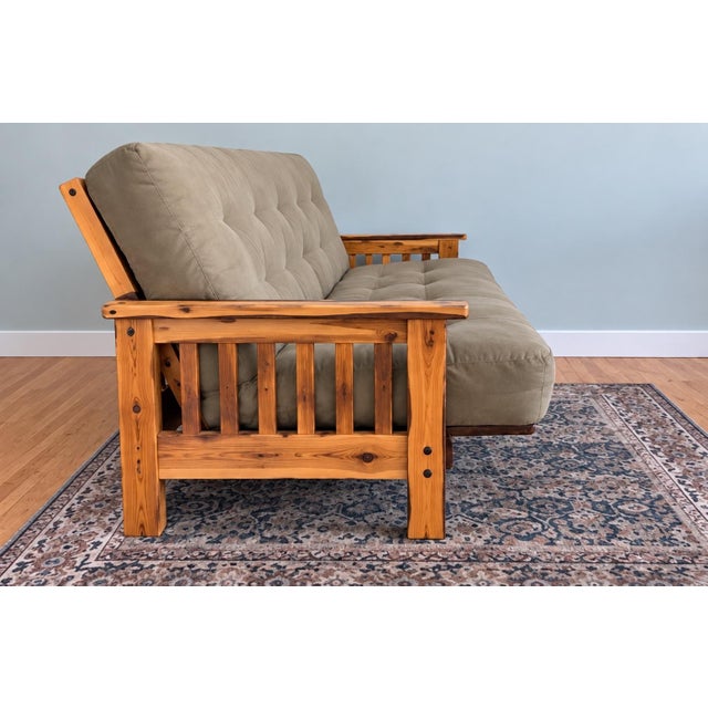 Charming rustic futon sofa featuring a substantial natural wood log frame with distinctive bark-edge detailing and...