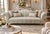 A classic upholstered sofa featuring a graceful camelback, sweeping scroll arms, and a continuous bench seat. It is...