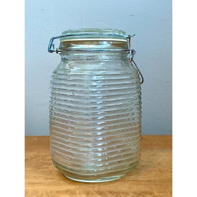 This vintage ribbed glass storage jar is a charming study in utilitarian design, its softly squared, gently tapered body...