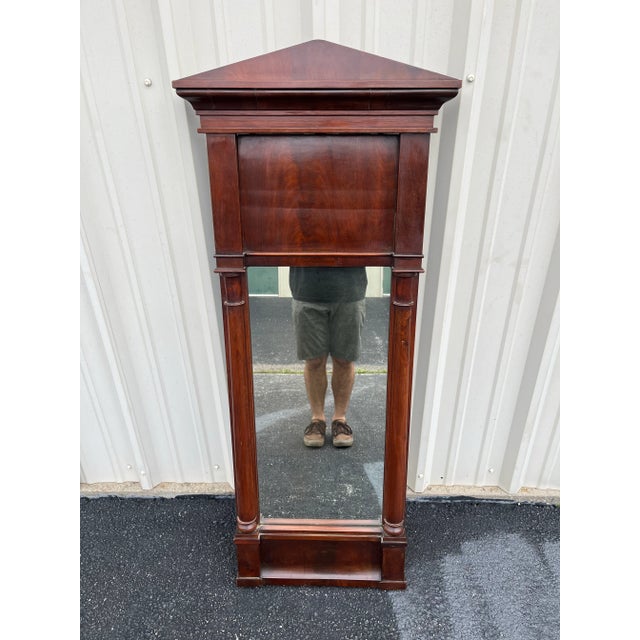 A stunning 19th century mahogany mirror in a neoclassical empire style. Tall and slender with a stout frame, this mirror...