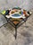 A striking vintage side table featuring a colorful stained glass top set within a sculptural wrought iron base. The...