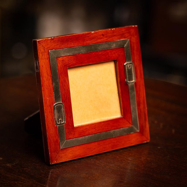 A 20th Century square picture frame in warm toned wood, accented with a brass band and distinctive buckle detail. Made in...