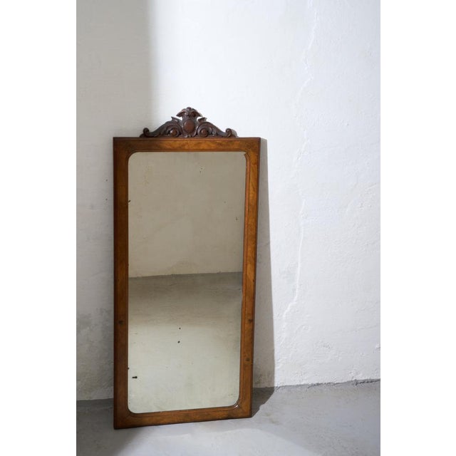 A refined wall mirror featuring a warm wooden frame and an elegantly carved crest detail. The clean proportions are...