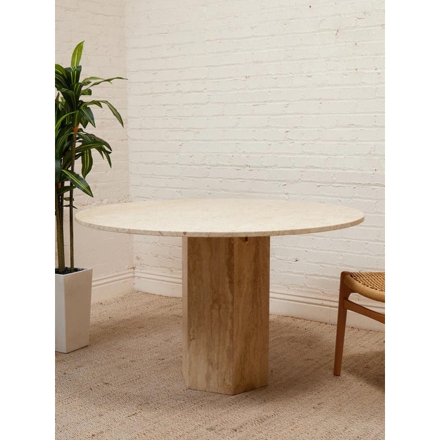 A beautifully sculptural modern dining table with a substantial round top and monolithic pedestal base finished in warm...