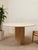 A beautifully sculptural modern dining table with a substantial round top and monolithic pedestal base finished in warm...