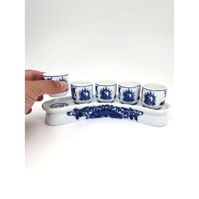 An eye-catching blue-and-white porcelain set featuring five shot-glasses and a beautifully curved matching stand, richly...