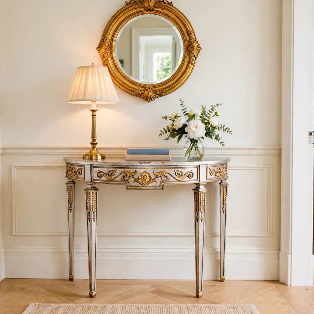 A sophisticated demilune console table by Maitland-Smith, featuring a Neoclassical silhouette and hand-applied distressed...