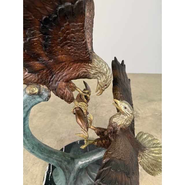 A bronze sculpture depicting two bald eagles engaged in an intense mid-air struggle over a freshly caught fish. With wings...