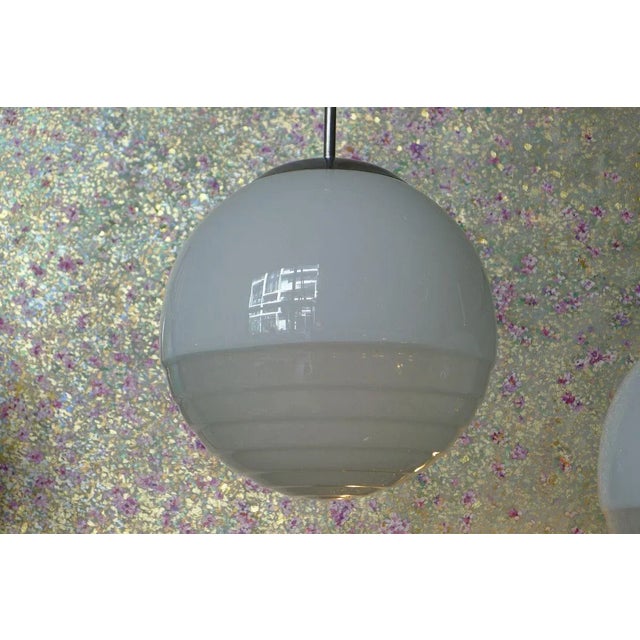 Pair of minimalist glass globe pendants. White in the upper segment, satinized lower part. The mountings vary a bit in the...