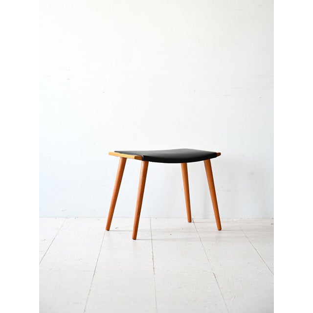 Vintage stool with birch wood structure and black imitation leather seat. Characterized by conical legs and the presence...