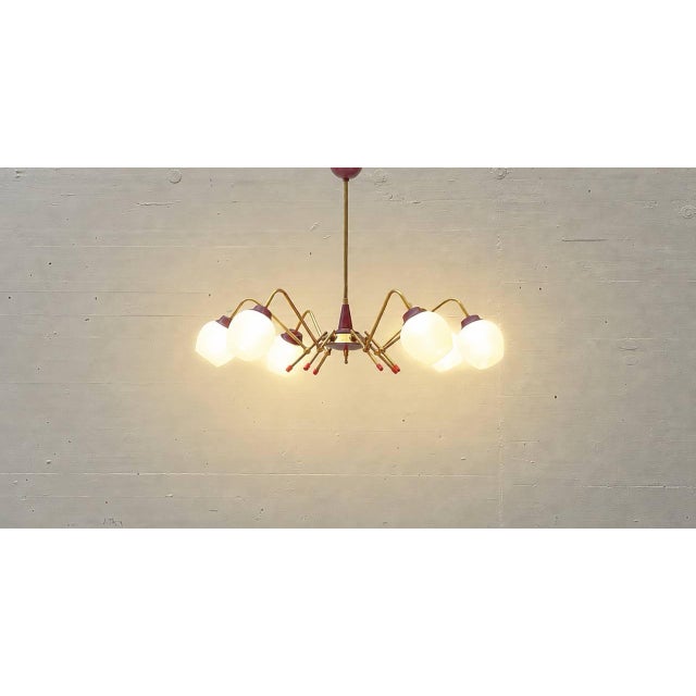 A striking Sputnik ceiling light from the 1950s, featuring a delicately curved brass frame and six opal white glass...