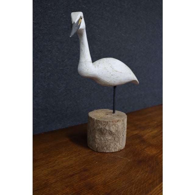 Hand-carved bird sculpture depicting a white heron with a long curved neck, slender dark bill, and yellow facial...