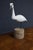 Hand-carved bird sculpture depicting a white heron with a long curved neck, slender dark bill, and yellow facial...