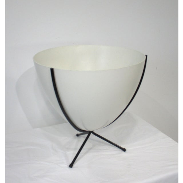 An off-white fiberglass Mid Century bullet planter with black iron tri pod base having rubber tips to the end legs to...