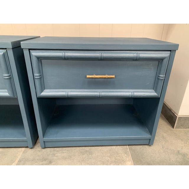 A vintage pair of faux bamboo nightstands painted in a soft grey blue. Original brassy, faux bamboo pulls on the drawers....