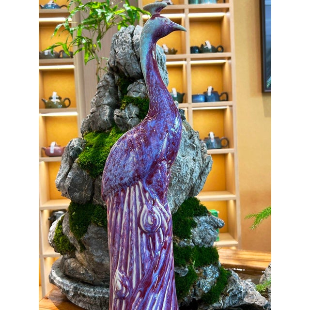 This striking ceramic sculpture depicts a standing peacock, a traditional symbol of beauty, dignity, and good fortune. The...