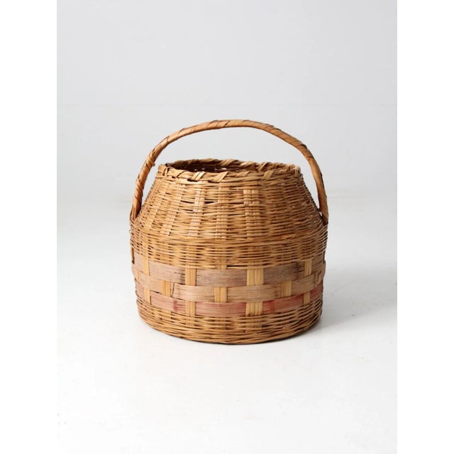 This is an antique market basket. The hand-woven basket features a pink stripe around the base and short carrying handle.