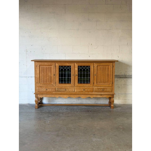 Grand architectural form features four carved doors including two leaded glass panels, four base drawers, and interior...