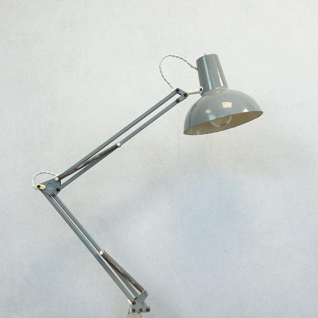 Grey architect's desk lamp with articulated double arm, weighted springs, and clamp-on base. Steel shade with perforated...