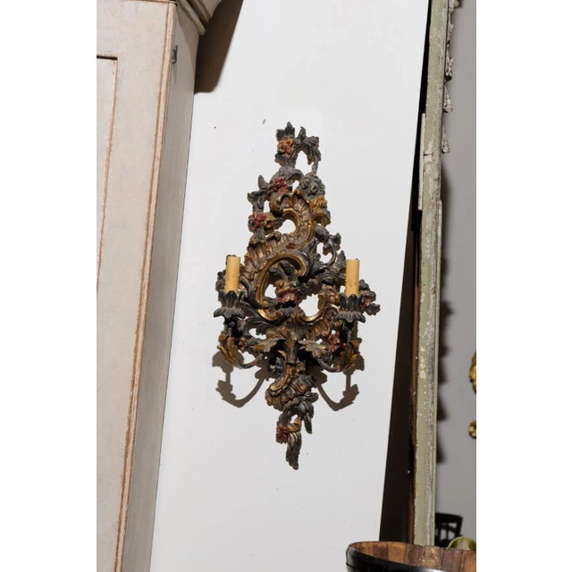 A pair of Italian Rococo style painted and carved, wood and metal two-light sconces from the late 19th century. Born in...