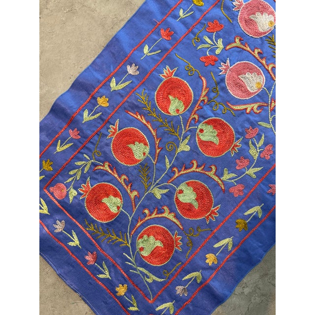 Hand-embroidered Suzani table runner from Uzbekistan — a red pomegranate vine climbing the length of a royal blue silk...