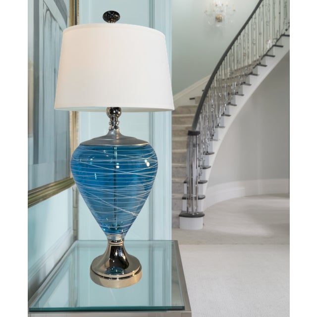This one‑of‑a‑kind table lamp features a substantial, curving body hand‑blown from aqua art glass by a skilled Seattle...