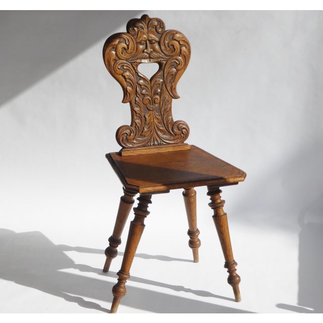 An antique folk art wooden chair with a carved face mask on the back rest made out of Alpine oak. The chair has 4 ankled...