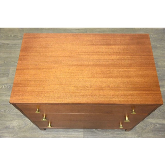 A mid century modern mahogany three drawer dresser chest with polished brass finger pulls manufactured by Widdicomb....