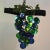 A bunch of large blue and green glass grapes hanging from a brown stem with several small light bulbs within the grapes,...