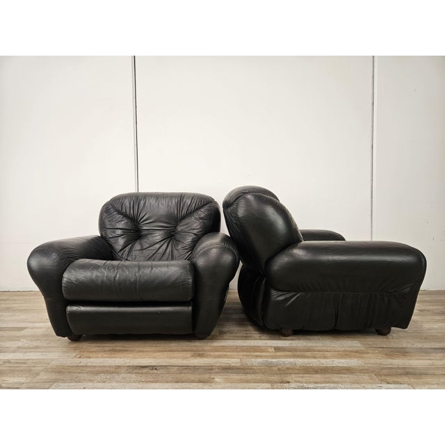 A pair of 1970s-style black leather armchairs, perfect for any setting thanks to their generous size and comfortable...