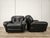 A pair of 1970s-style black leather armchairs, perfect for any setting thanks to their generous size and comfortable...