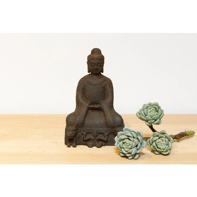 A captivating antique rusted metal Buddha figure. The cast seated Buddha rests on a rectangular base adorned with two...