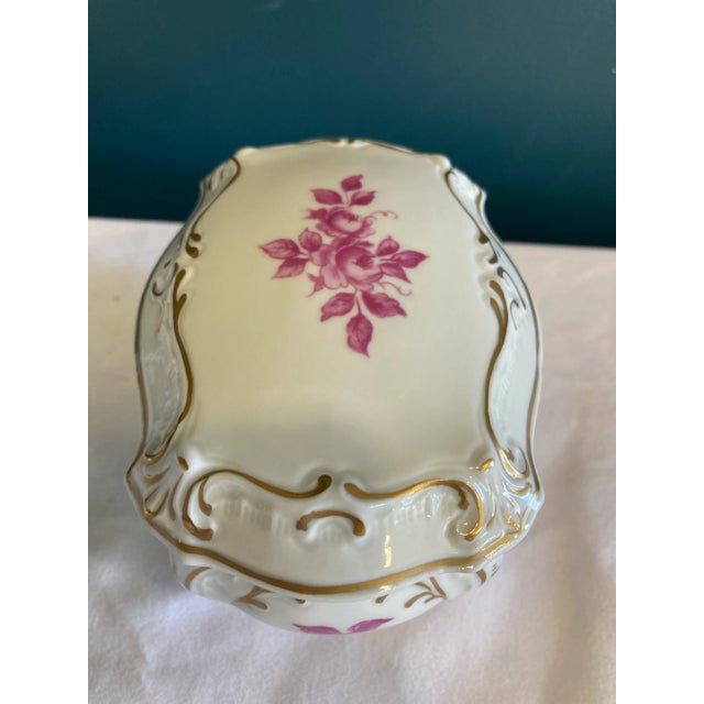 This refined vintage porcelain trinket box showcases a pristine white body adorned with exquisite gold trim and delicate...