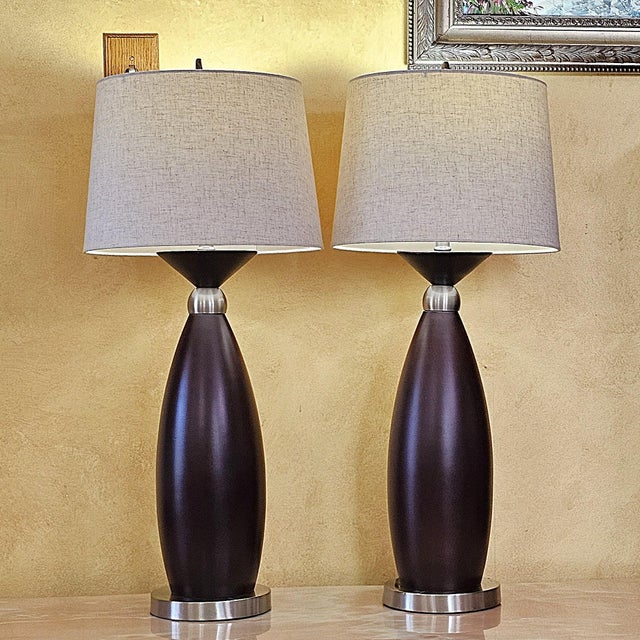 Pair of contemporary hourglass-form table lamps featuring espresso wood-look bodies, brushed nickel-tone accents and...