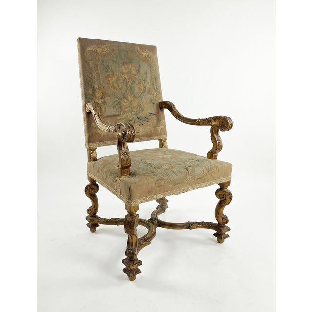 A richly detailed Louis XIV armchair featuring hand-carved scroll arms, acanthus leaf legs, and a serpentine stretcher...