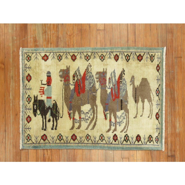 A mid 20th century hand-knotted Turkish Rug with 3 brown camels hooked on a small black horse and a human figure Details...
