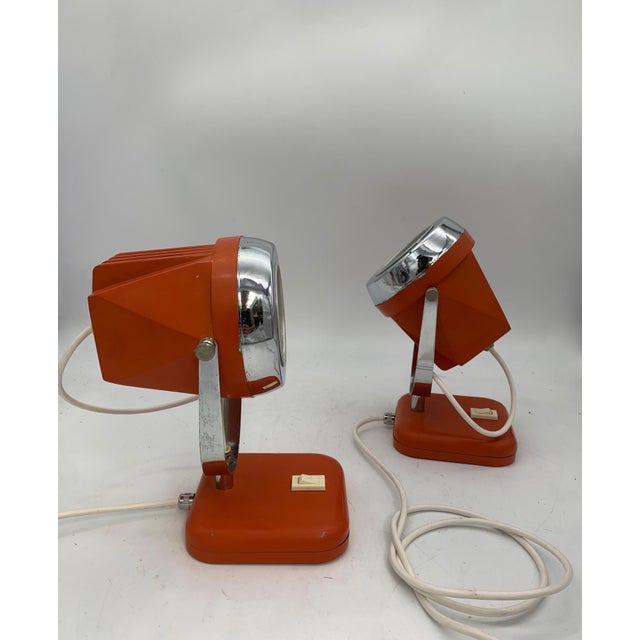 A pair of 1970s-style adjustable space-age table lamps, featuring a conical body in orange lacquered metal and a polished...
