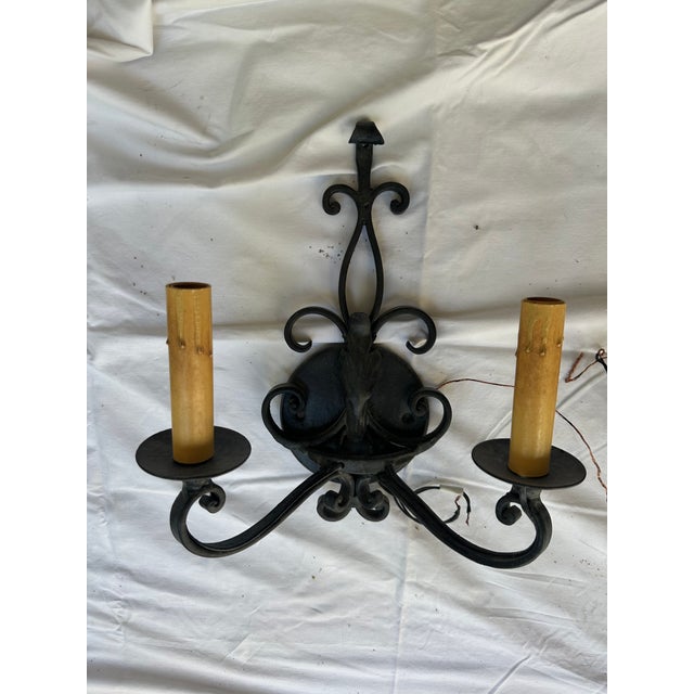Matching set of black wrought iron two arm sconces with scrollwork backplates and beeswax-style candle covers.