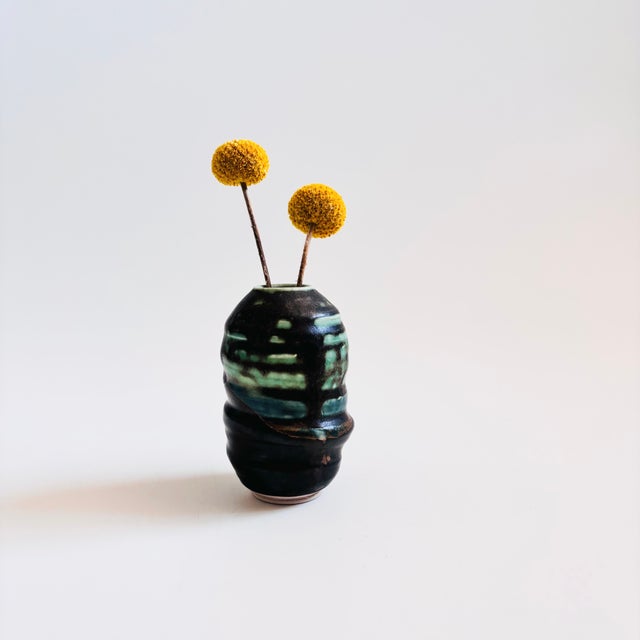 A vintage studio pottery bud vase. Irregular cylinder form with a small opening on the top. Finished in green and black...
