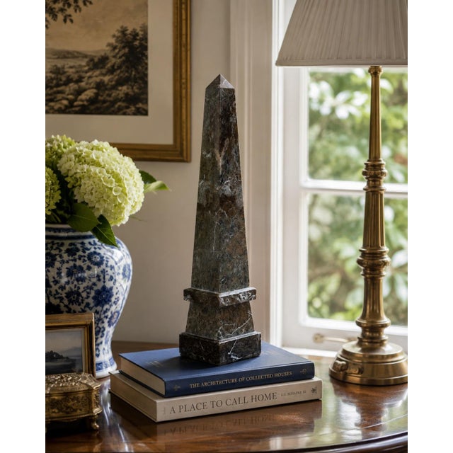 A beautifully proportioned marble obelisk in richly veined shades of black, brown, and gray. The sculptural silhouette and...