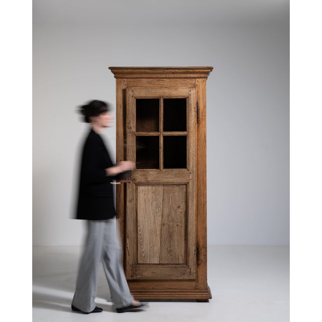 A tall Provençal oak vitrine reflecting the rustic elegance of southern French countryside interiors. The glazed upper...