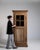 A tall Provençal oak vitrine reflecting the rustic elegance of southern French countryside interiors. The glazed upper...