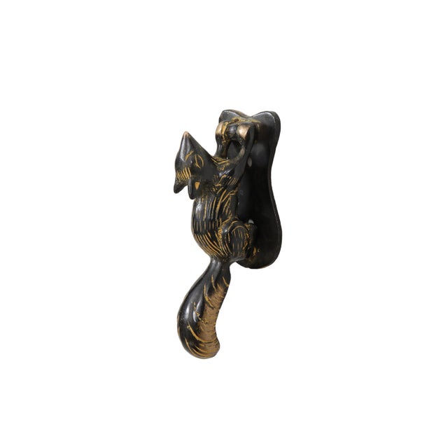 A black and yellow brass door knocker shaped like a squirrel. Cast in a listening pose with a prominent tail, finished...
