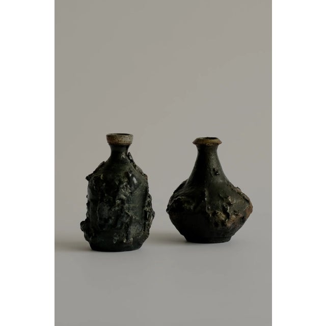 A pair of small, hand-formed brutalist vessels defined by their irregular, raw and elemental surface and sculptural...