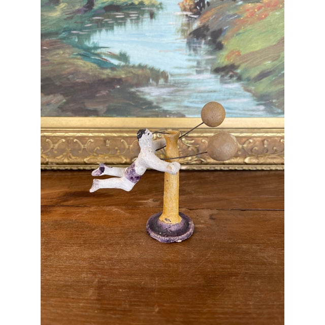 This antique possibly clay toy features a hand-painted strongman figure performing an acrobatic pose with two spherical...