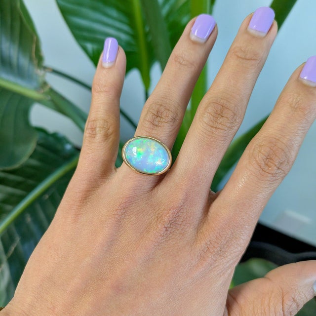 A large 7.75-carat Ethiopian opal cabochon flashes with a full play of colour across this solid 14K yellow gold ring....
