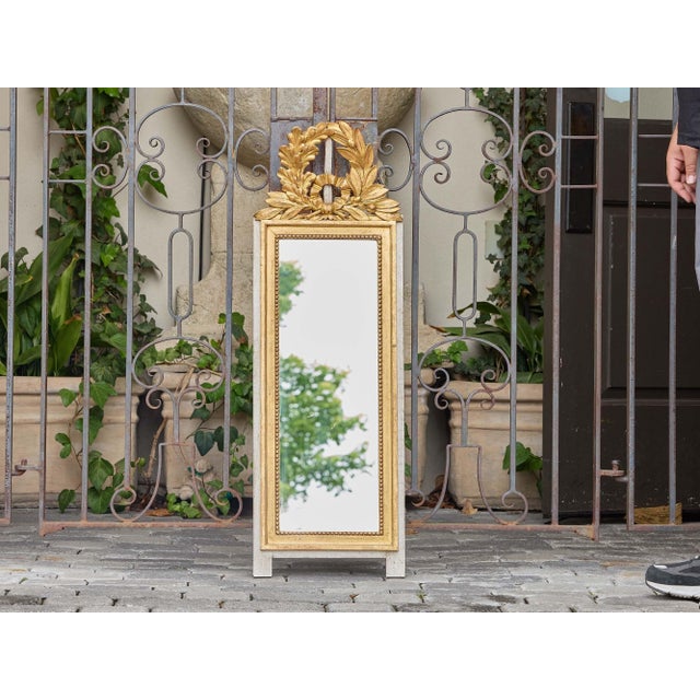 This French Louis XVI revival giltwood mirror from circa 1920 presents a refined, neoclassical aesthetic anchored by a...