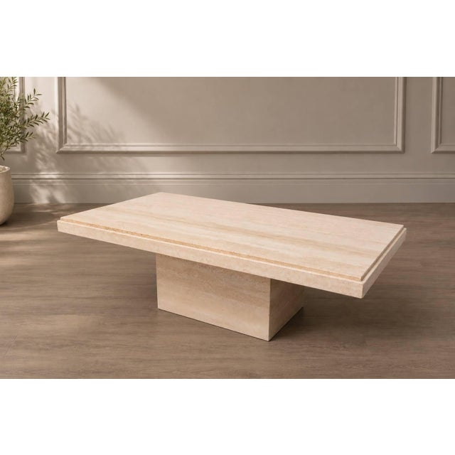 A substantial travertine coffee table with a clean rectangular top and solid pedestal base. The natural stone has...