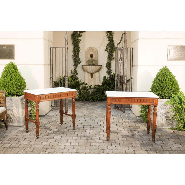 A pair of French neoclassical style wooden console tables from the late 19th century, with white marble tops. Crafted...