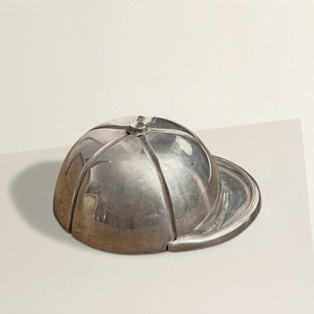 At first glance, it’s a polished little keepsake — a vintage English silver-plate jockey’s helmet, gleaming softly on the...